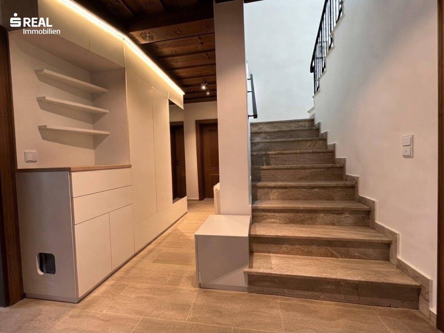 Heller Eingangsbereich mit moderner Garderobe, Steinfliesenboden und Treppe zum Obergeschoss.