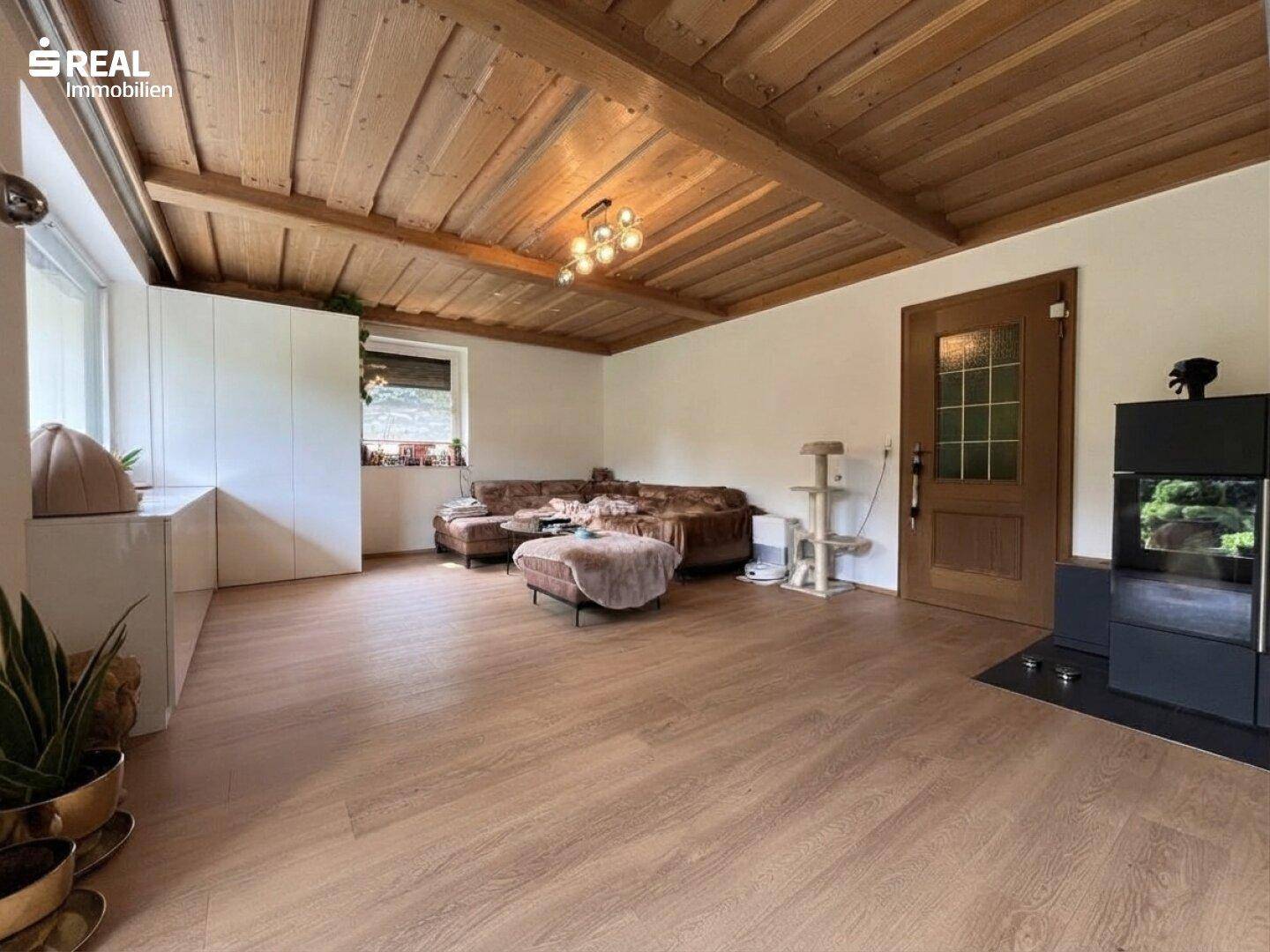 Gemütliches Wohnzimmer mit Holzbalkendecke, Laminatboden und einem modernen Kaminofen.