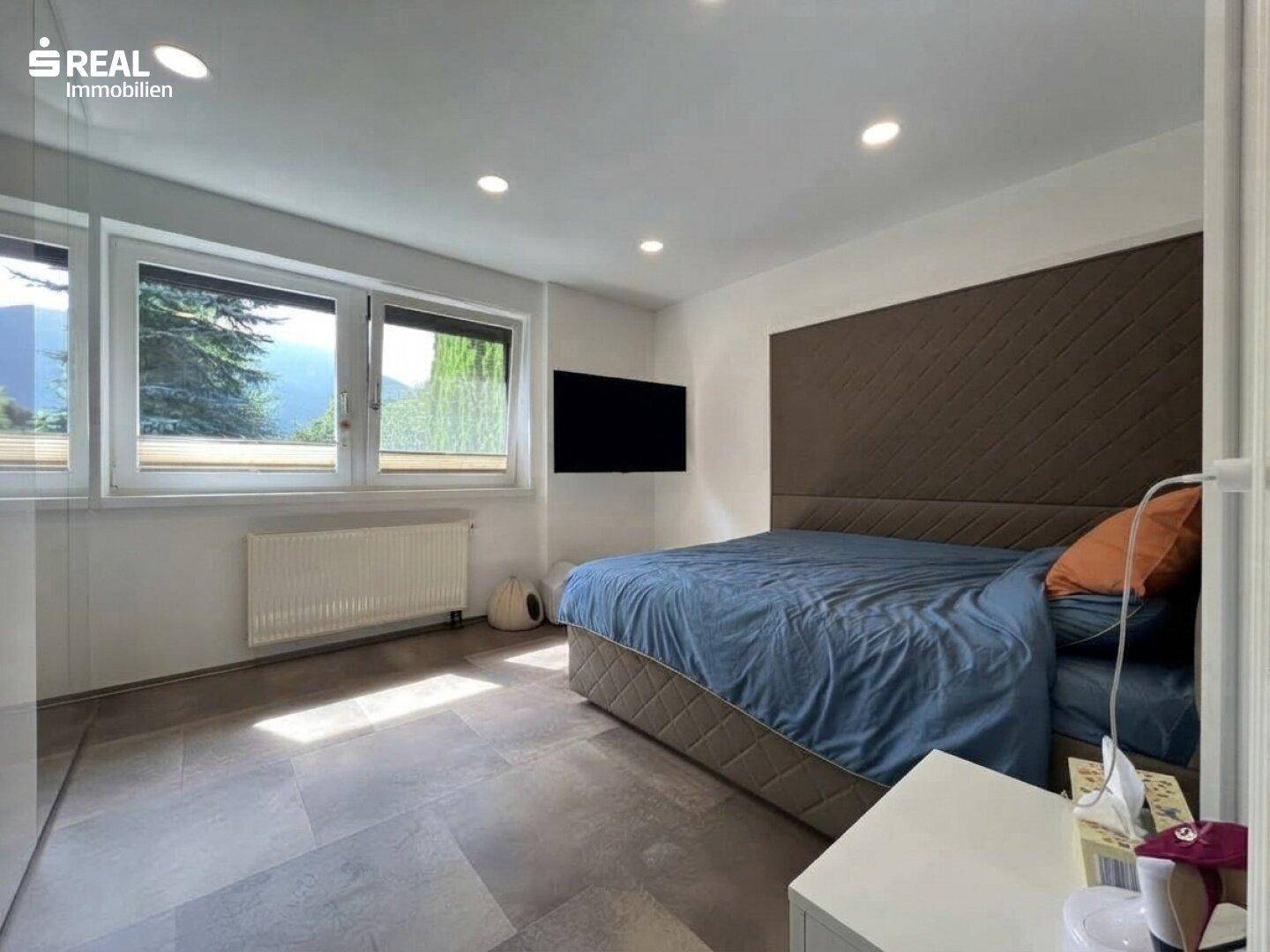 Modernes Schlafzimmer mit großem Bett, Einbaustrahler und Blick auf die umliegende Natur.