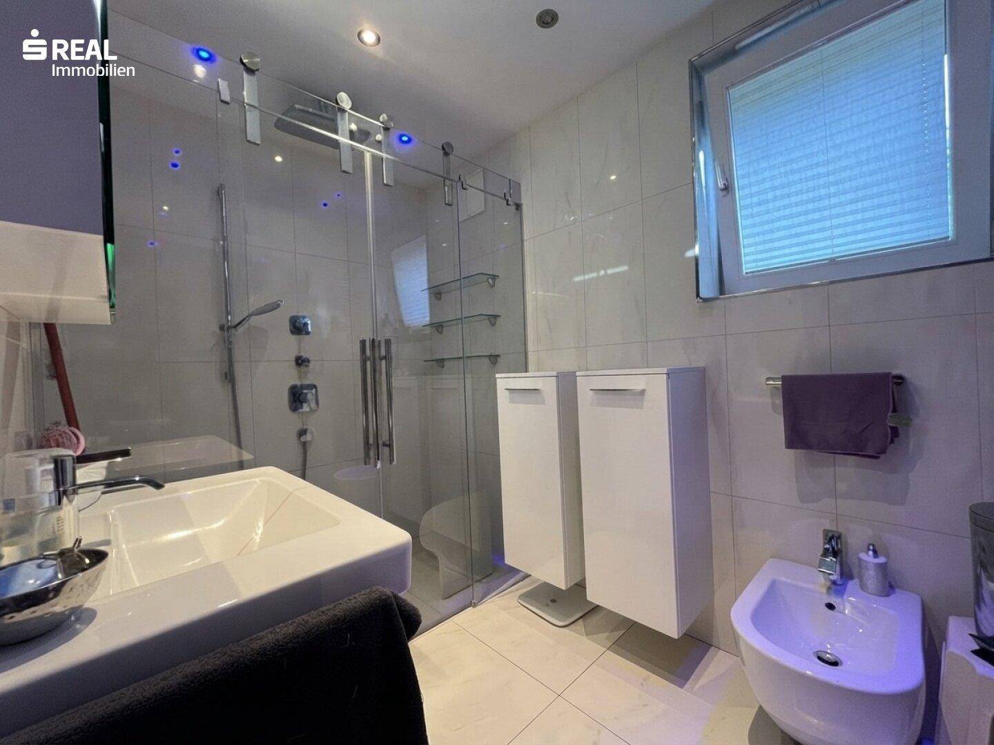 Modernes Badezimmer mit großer Glasdusche, Bidet und Einbauschränken in Weiß.