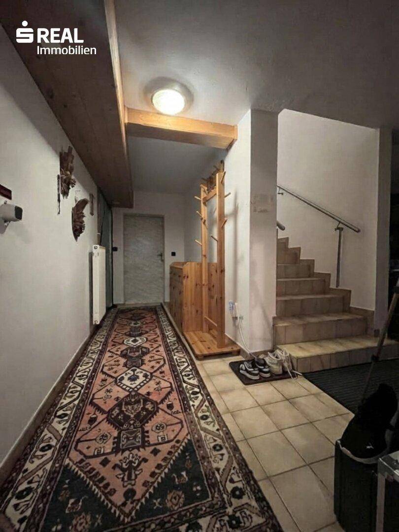 Geräumiger Flur mit Teppichläufer, Holzgarderobe und Treppe zum Obergeschoss.