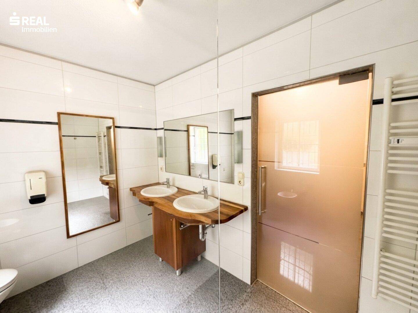 Modernes Badezimmer mit Doppelwaschbecken, großen Spiegeln und weiß gefliesten Wänden.