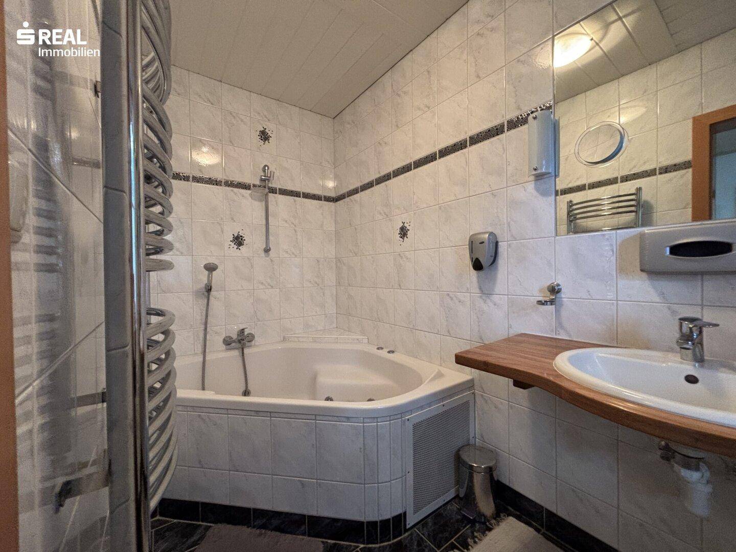 Gefliestes Badezimmer mit Eckbadewanne, Dusche und beheiztem Handtuchhalter.