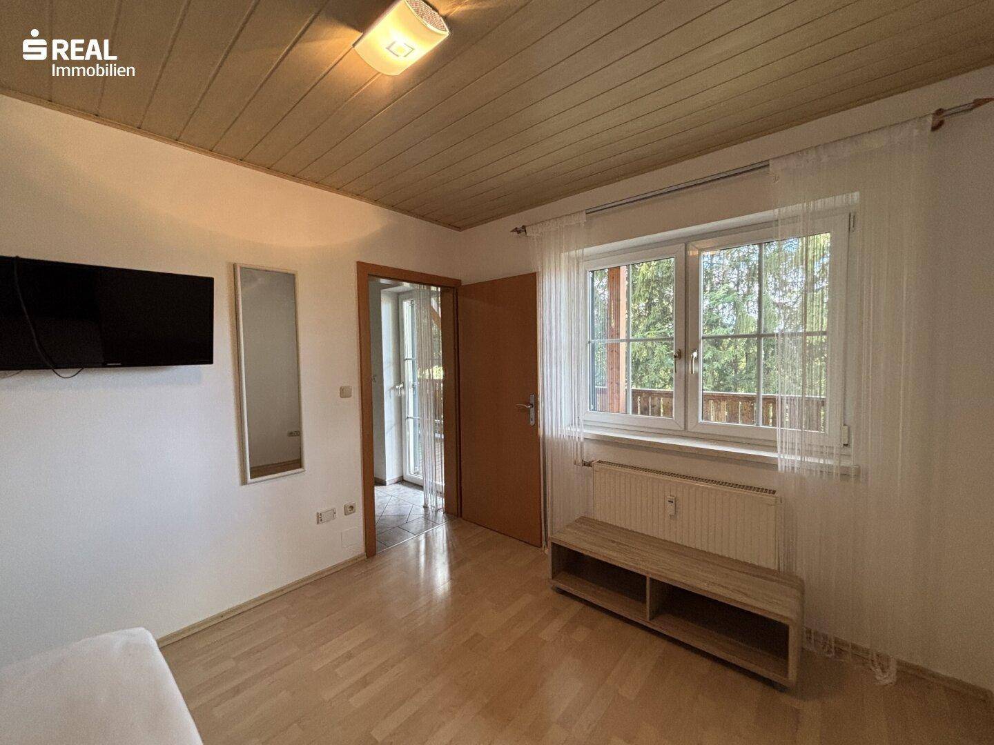 Gemütliches Schlafzimmer mit großem Fenster, Holzboden und Zugang zum Balkon.