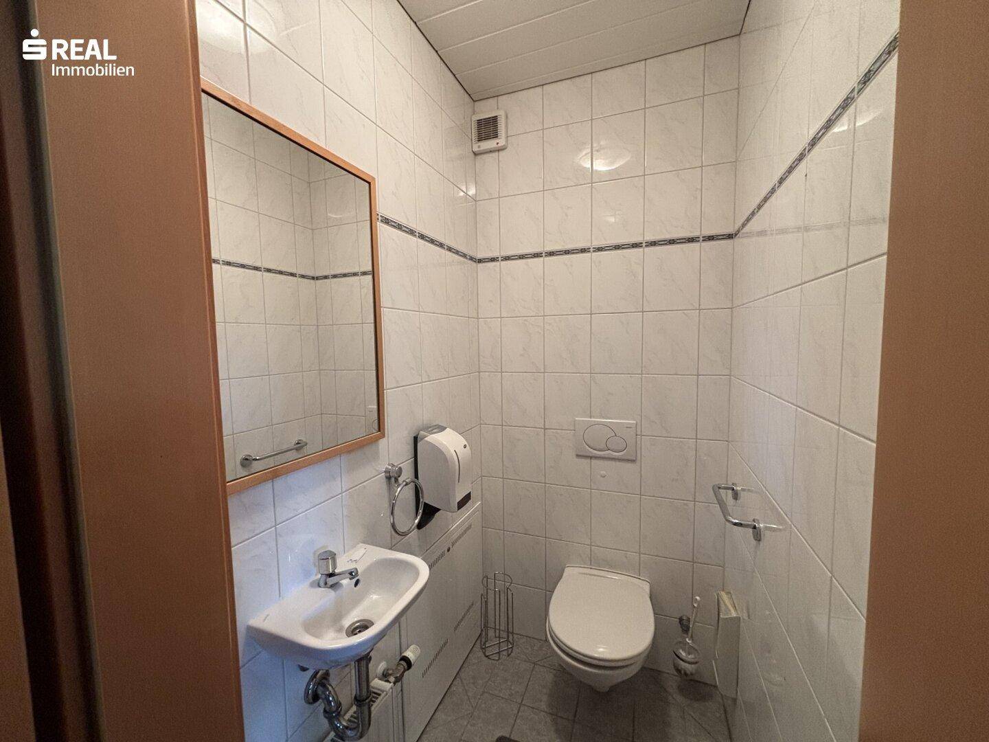 Separates WC mit Waschbecken, Spiegel und weißen Fliesen, funktional und sauber.