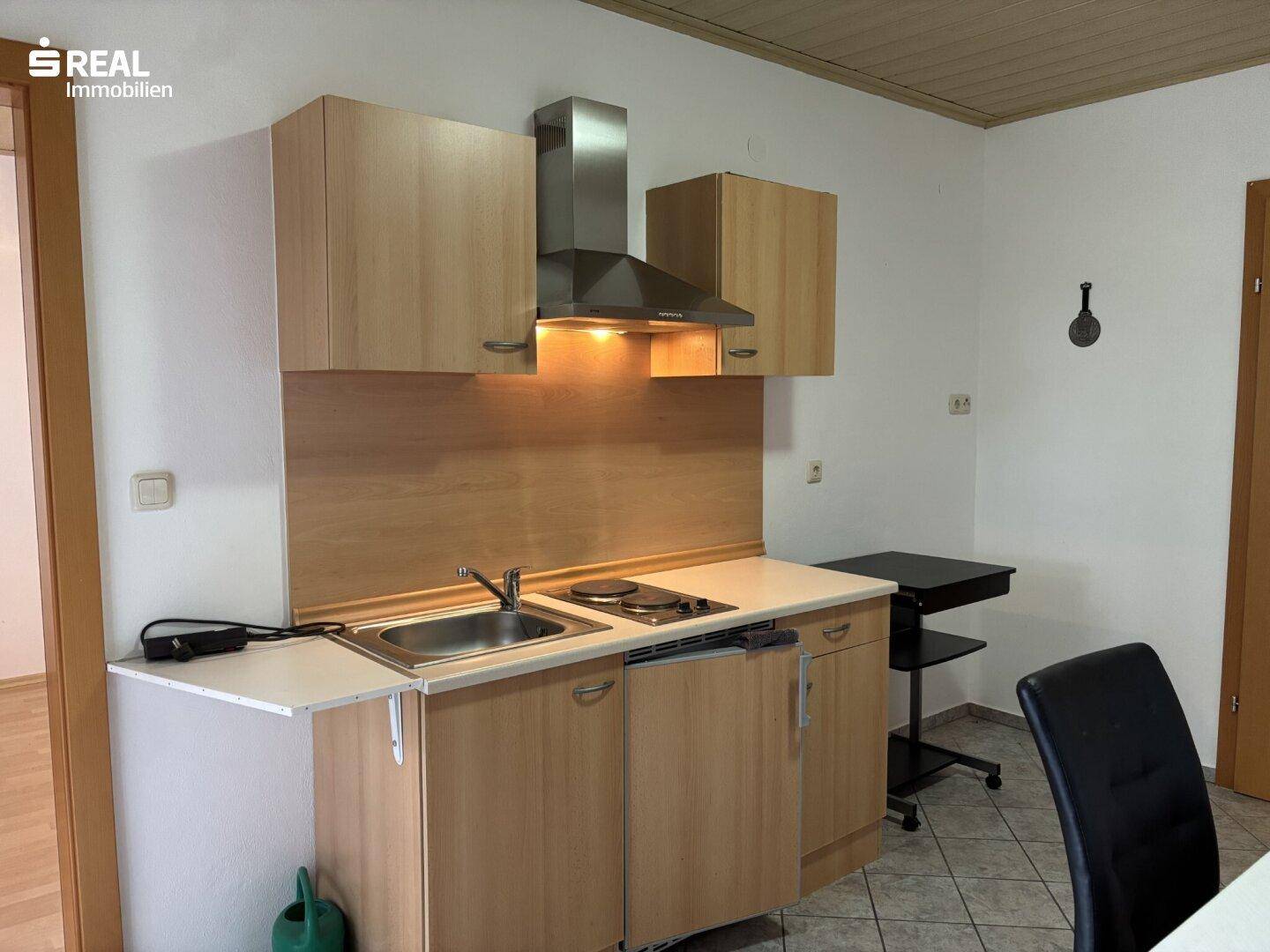 Kompakte Küchenzeile mit Spüle, Kochfeld und Dunstabzugshaube in hellem Holzdesign.