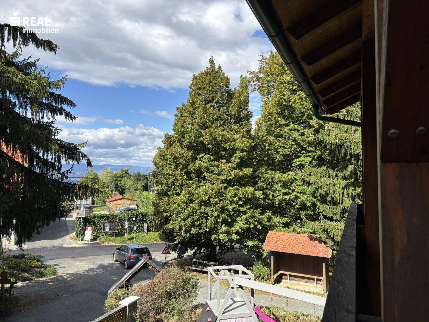 Weitläufiger Blick auf die grüne Umgebung mit Bäumen und einem kleinen Spielplatz.