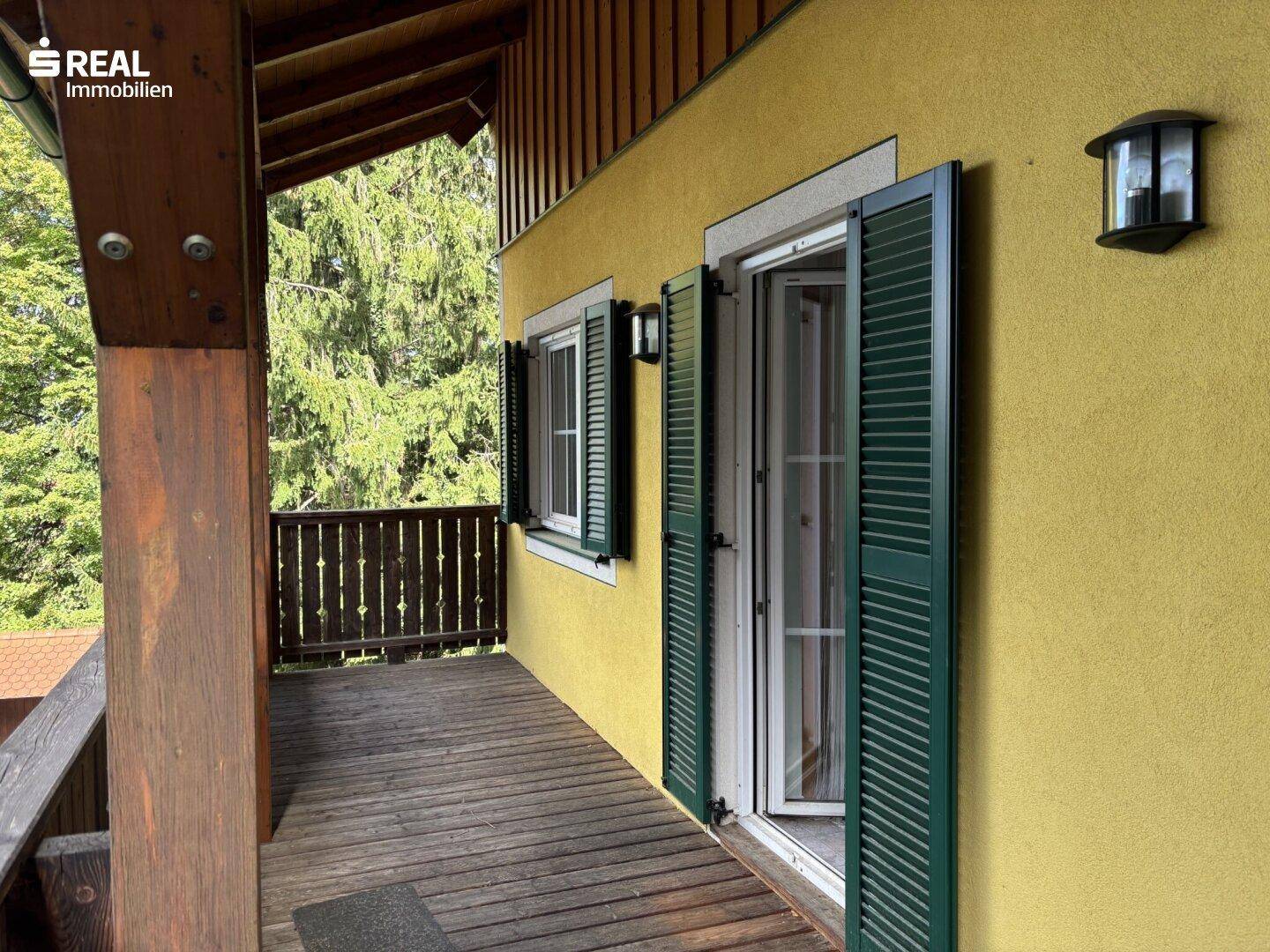 Langer, überdachter Balkon mit Holzboden und Blick ins Grüne, ideal zum Entspannen.