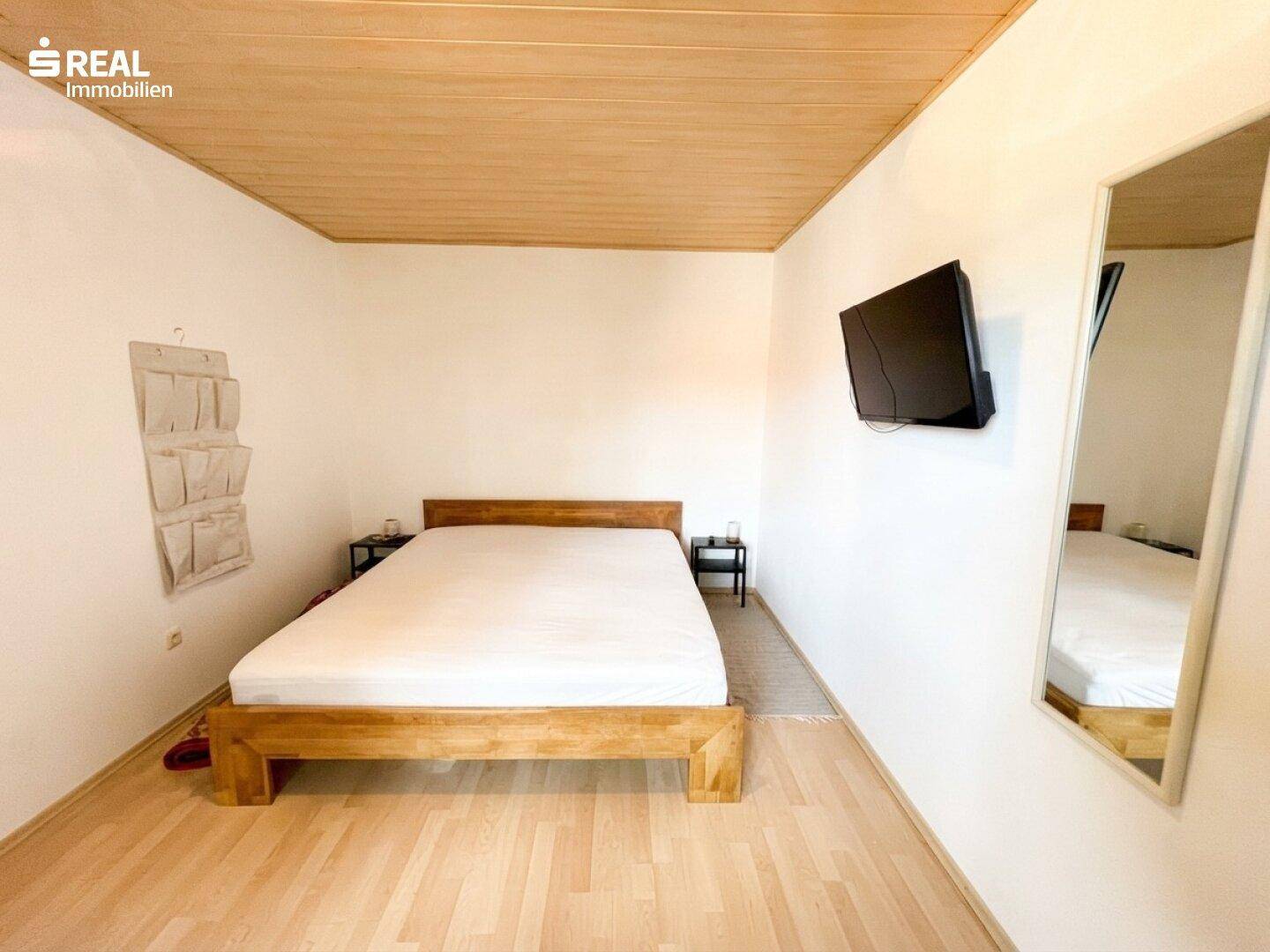 Helles Schlafzimmer mit Holzbett, Holzdecke und Parkettboden, modern eingerichtet.