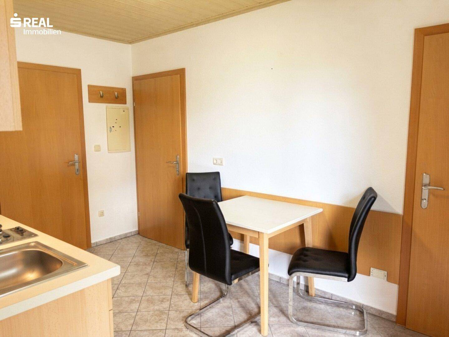 Essbereich in der Küche mit einem kleinen Tisch und zwei Stühlen, umgeben von Holztüren.