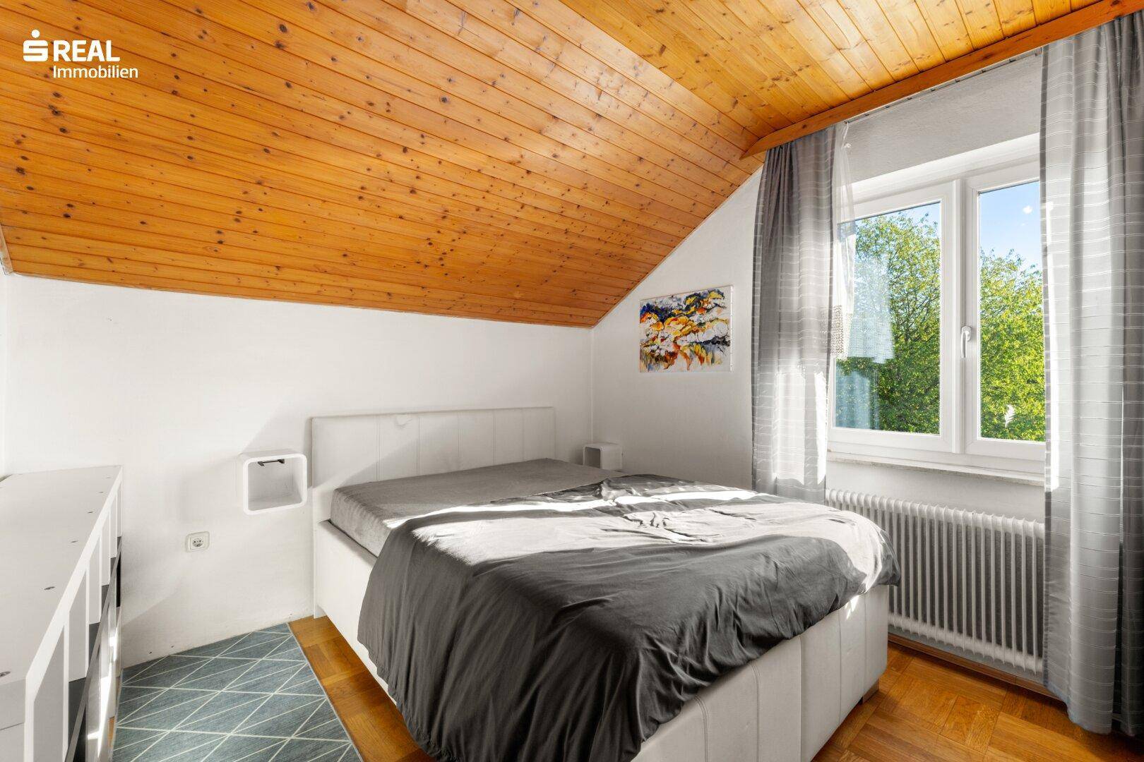 Gemütliches Schlafzimmer mit Holzdachschräge, Doppelbett und Fensterblick ins Grüne.