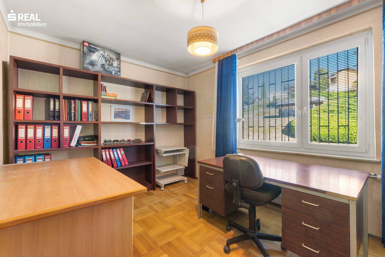 Arbeitszimmer mit Holzregalen, Schreibtisch und Fenster mit Blick nach draußen.