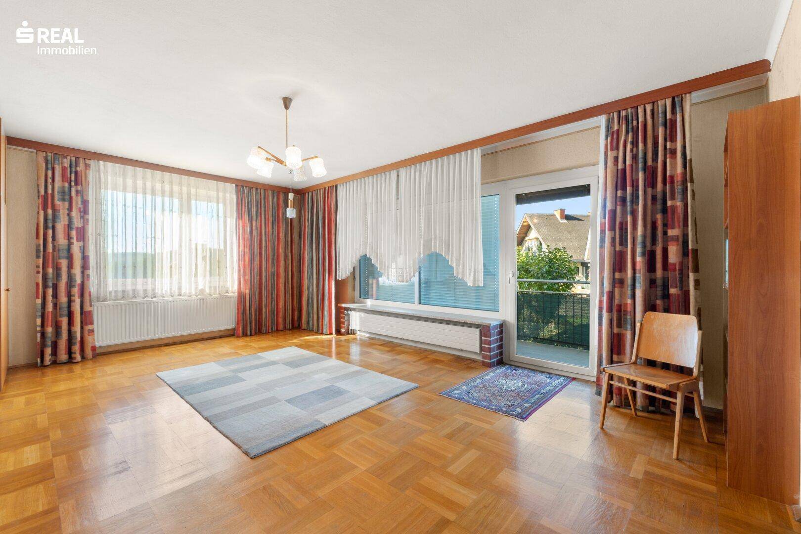 Geräumiges Wohnzimmer mit Parkettboden, großen Fenstern und Zugang zum Balkon.