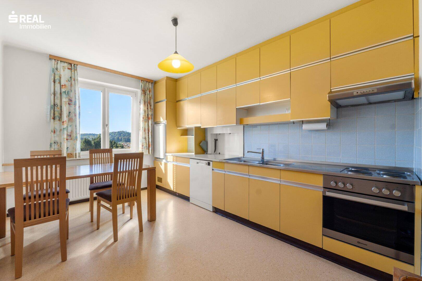 Geräumige Küche mit gelben Schränken, Essbereich und Fenster mit viel Tageslicht.