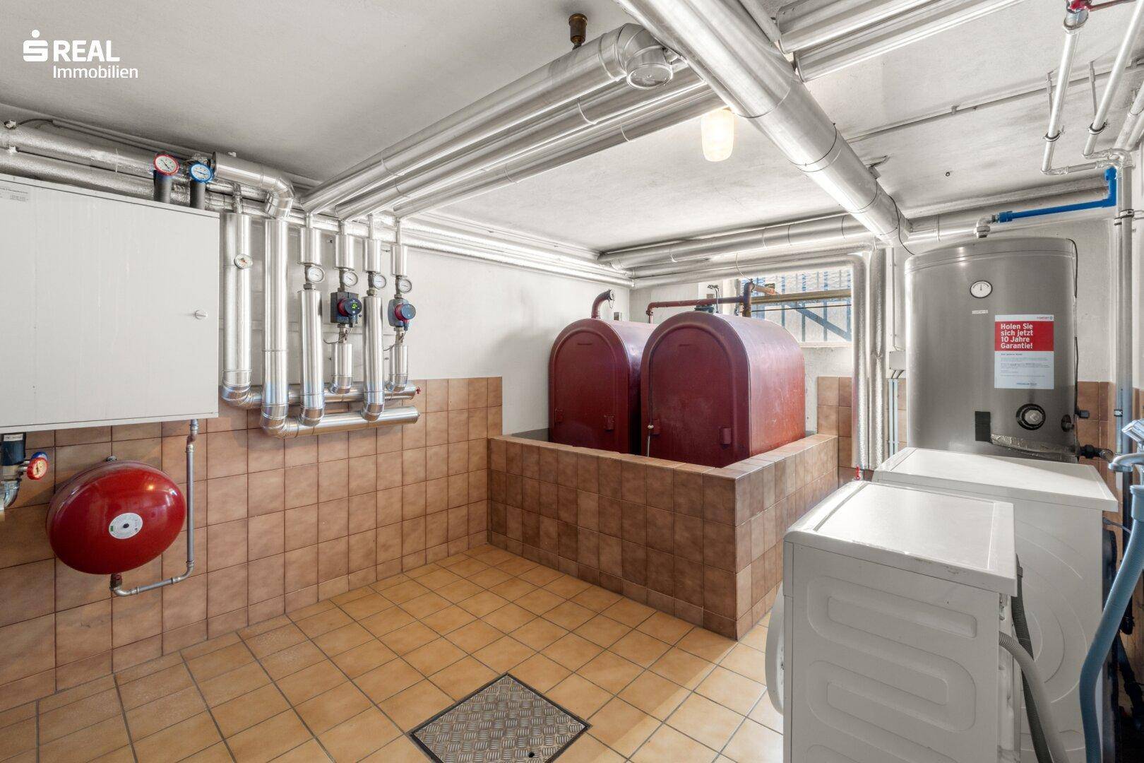 Heizraum im Keller mit Heizungsanlage, Öltanks und Waschmaschine auf Fliesenboden.