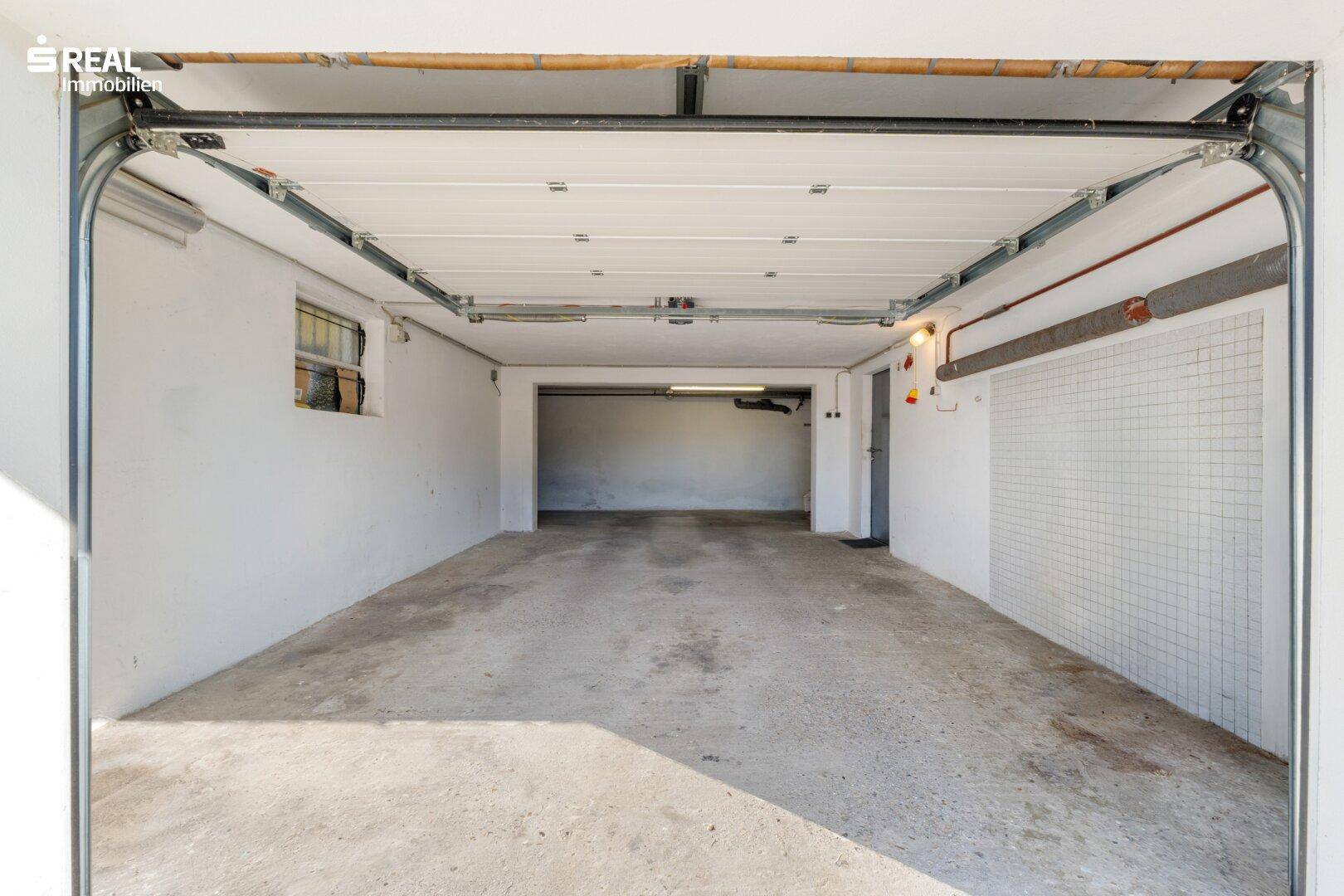 Leere Garage mit Rolltor und Fenster, bietet Platz für ein Fahrzeug.