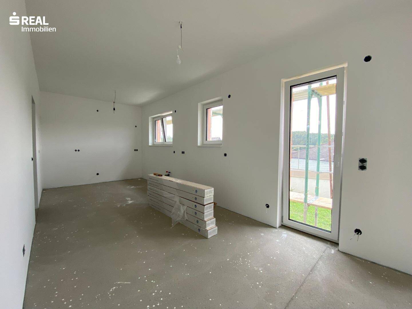 Heller Raum im Neubau mit Rohbetonboden und mehreren Fenstern für viel Tageslicht.