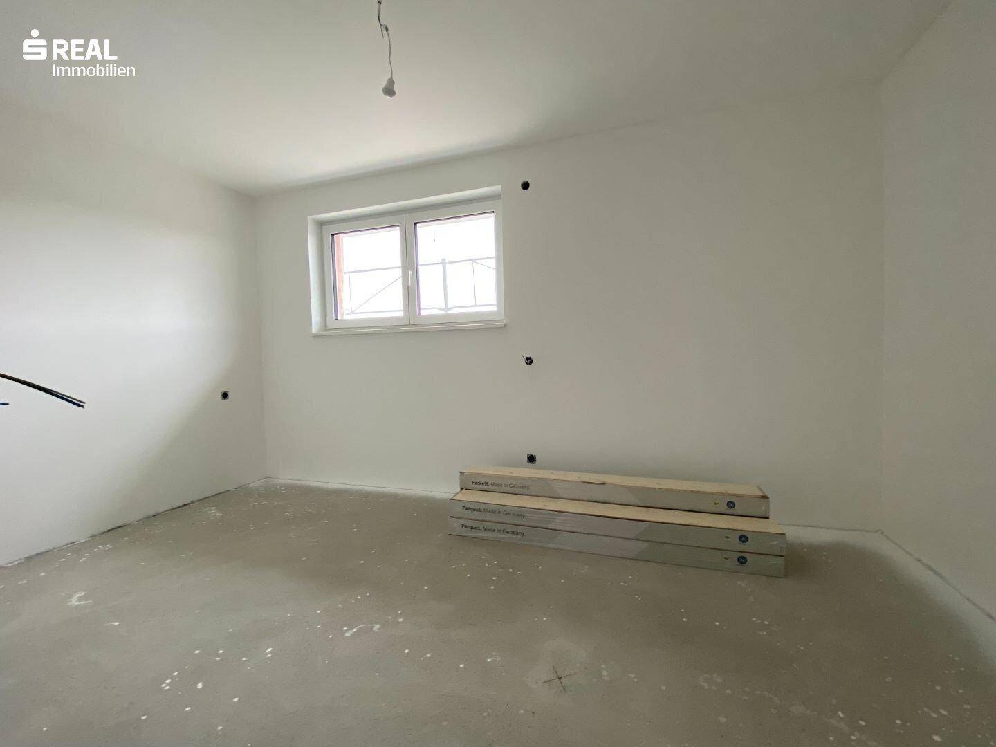 Schlafzimmer im Neubau mit Rohbetonboden, weiß gestrichenen Wänden und einem Fenster.