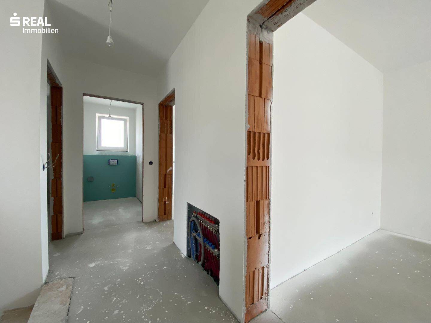 Flur im Neubau mit sichtbaren Installationsvorbereitungen und Zugang zu weiteren Räumen.