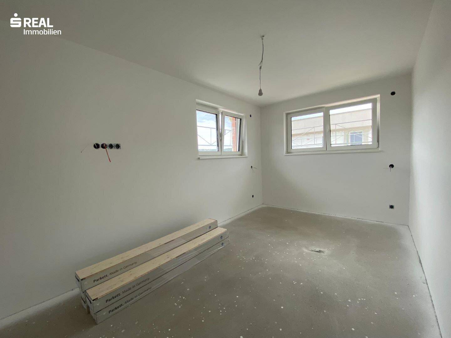 Weiteres Schlafzimmer im Neubau mit Rohbetonboden und zwei Fenstern für gute Belichtung.