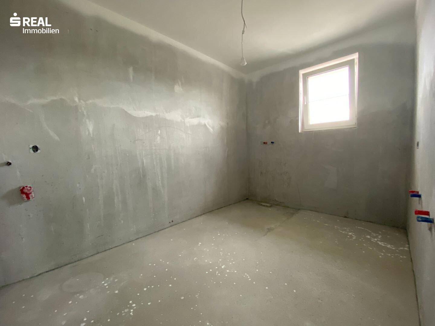 Badezimmer im Rohbau mit grauen Wänden, Rohbetonboden und vorbereiteten Sanitäranschlüssen.