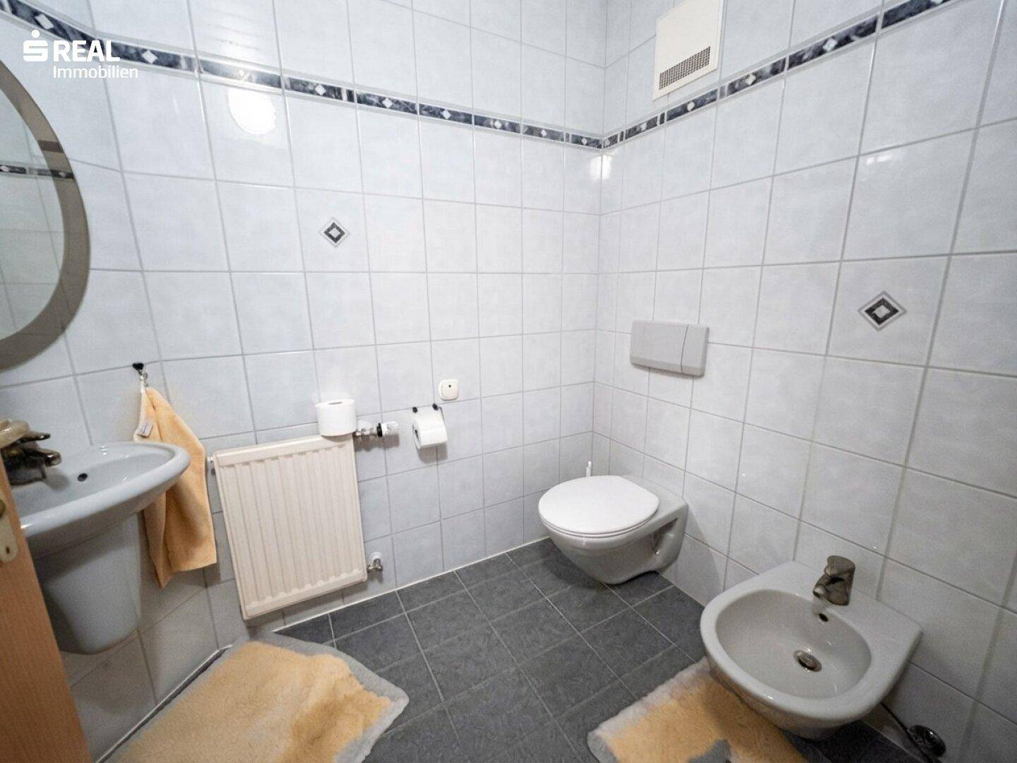 Kleines Badezimmer mit weißen Fliesen, WC, Waschbecken und Bidet.