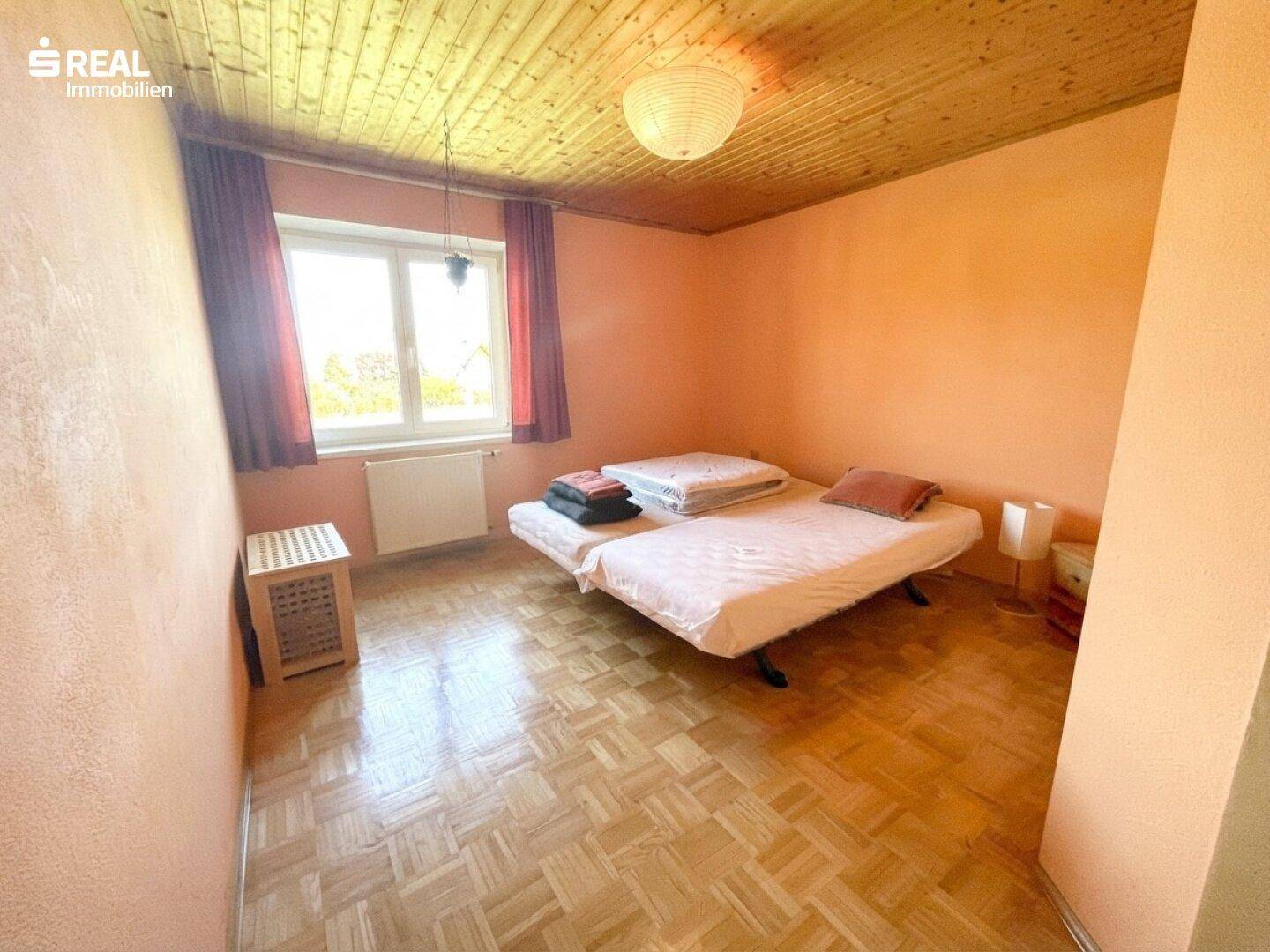 Schlafzimmer mit Holzdecke, Parkettboden und zwei Einzelbetten.