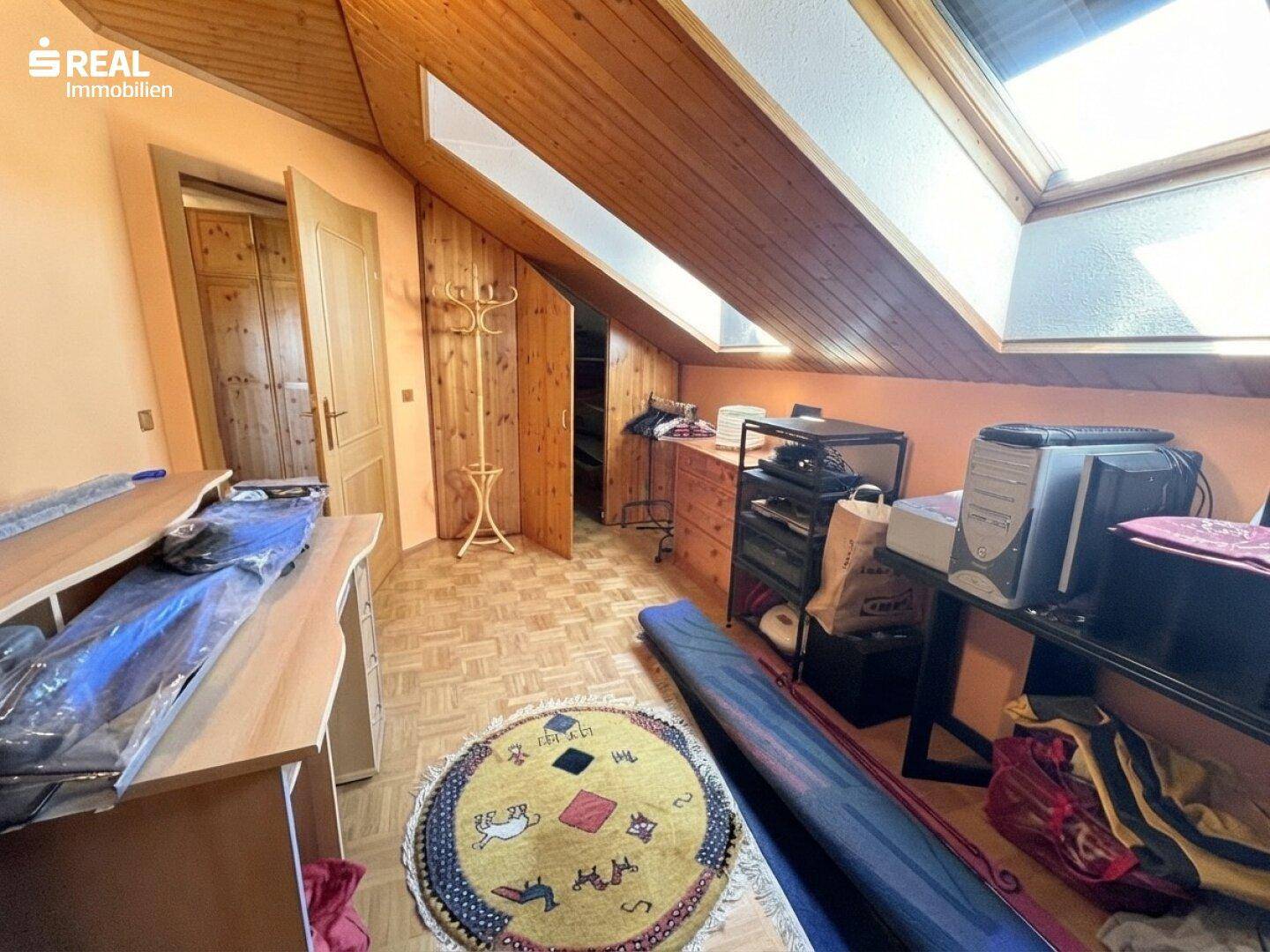 Dachgeschossraum mit Holzverkleidung, Dachschrägen und Dachfenstern, genutzt als Abstellraum.