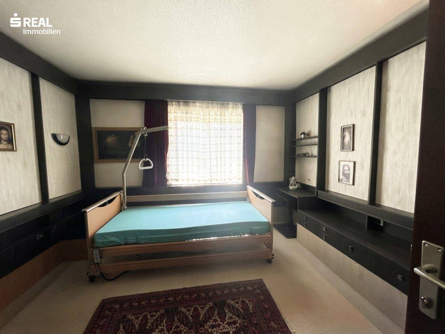 Schlafzimmer mit Pflegebett, dunklen Einbauschränken und Teppichboden.