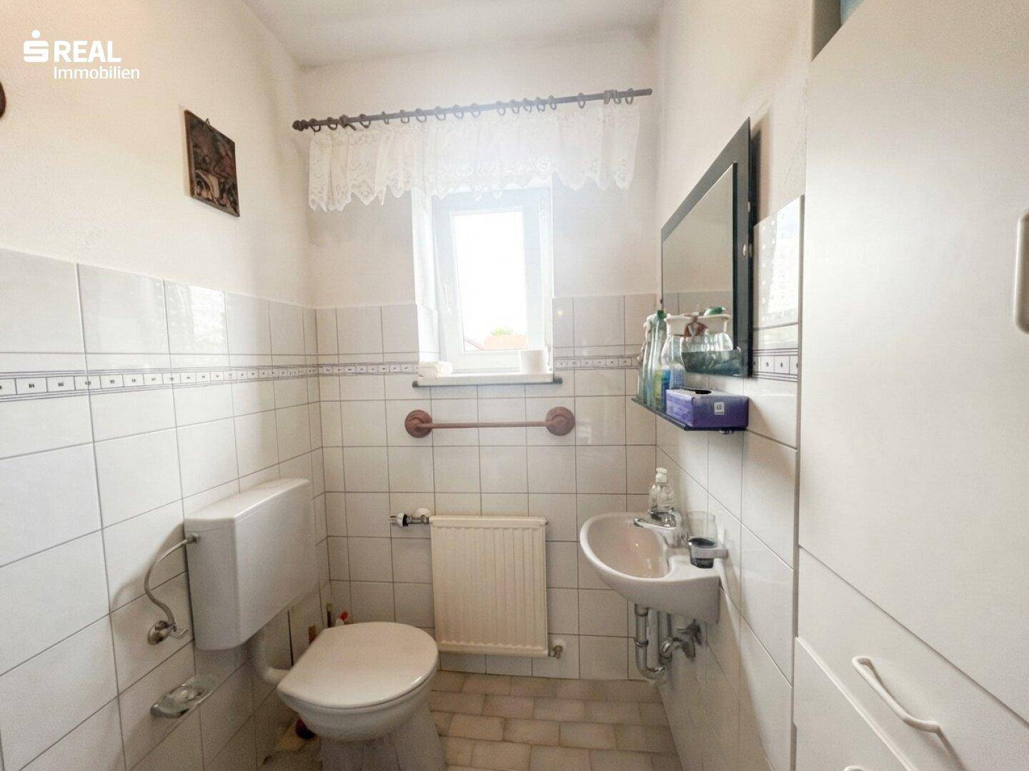 Kleines Gäste-WC mit Fenster, weißen Fliesen und Waschbecken.