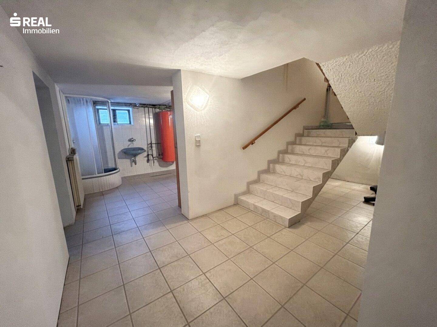 Kellerflur mit gefliester Treppe und Zugang zu weiteren Kellerräumen.