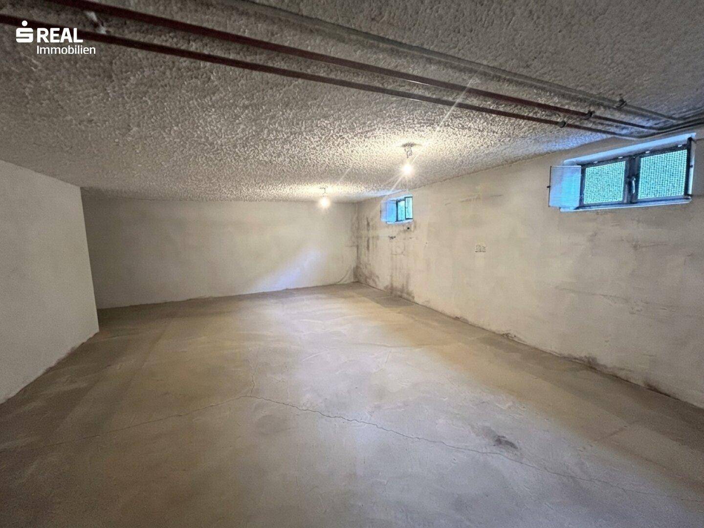 Großer, unfertiger Kellerraum mit Betonboden und kleinen Fenstern.