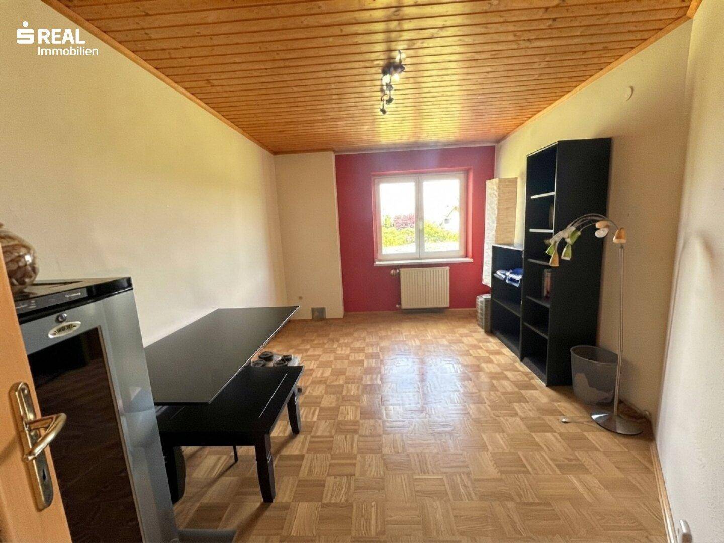 Geräumiger Raum mit Holzdecke, Parkettboden und roter Akzentwand.