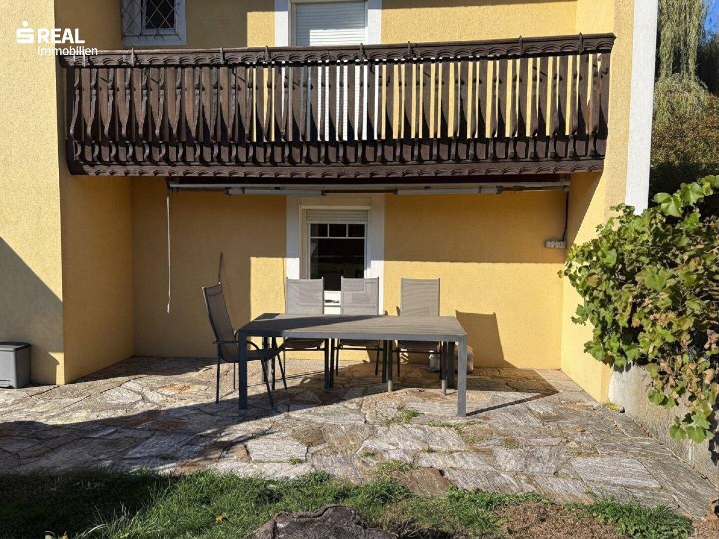 Gepflasterte Terrasse mit Gartenmöbeln und Blick auf den Balkon des Hauses.