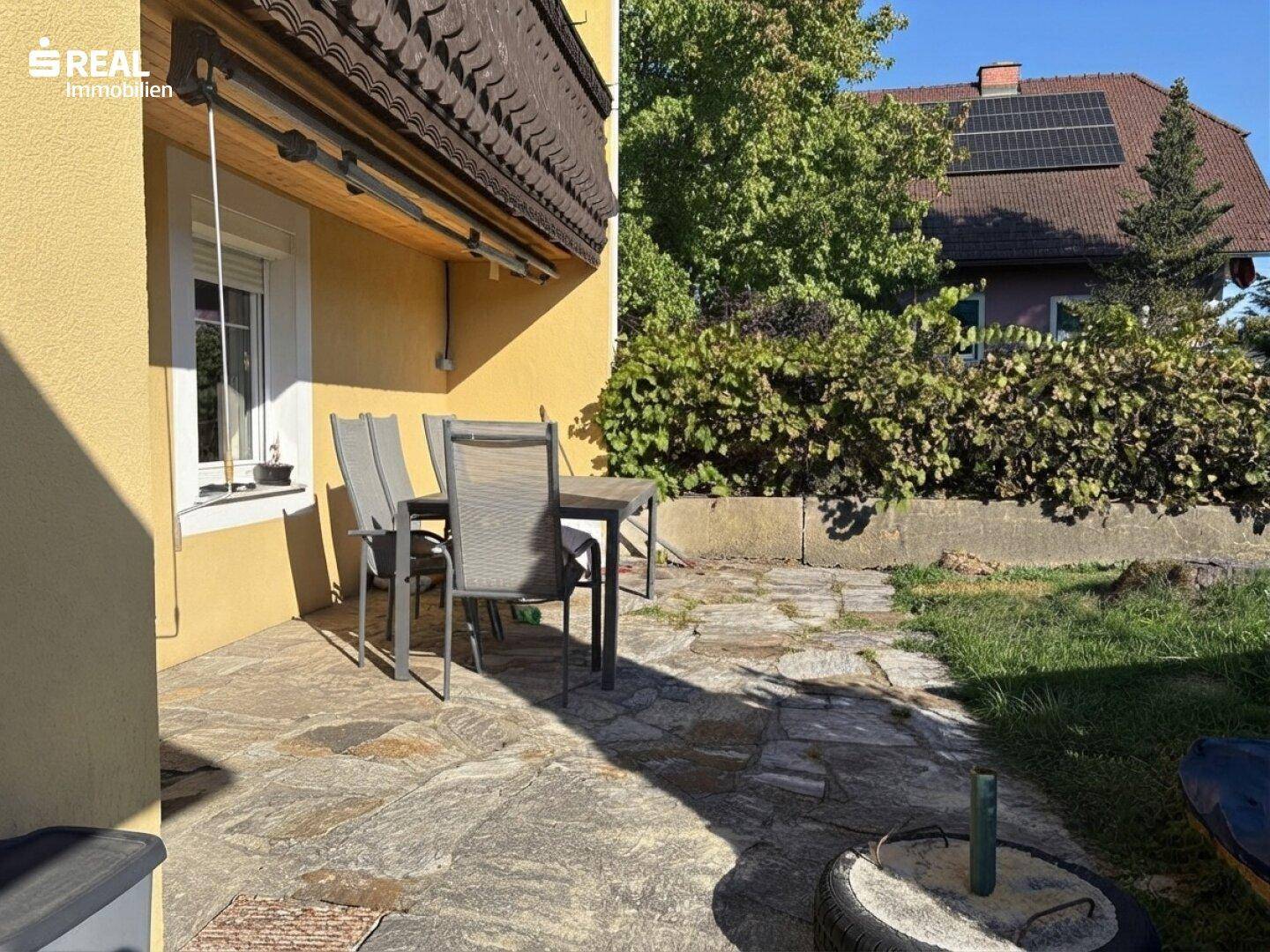 Sonniger Terrassenbereich mit Steinfliesen und angrenzendem Rasen, ideal für Entspannung im Freien.