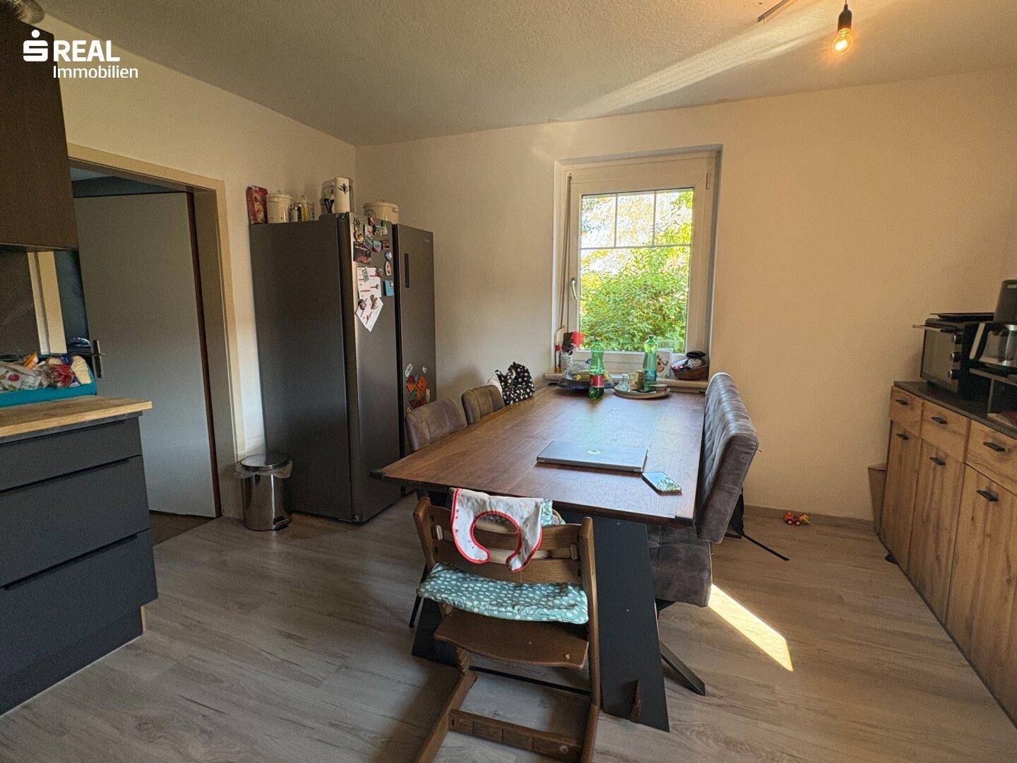 Geräumiger Essbereich mit großem Holztisch und Blick ins Grüne durch das Fenster.