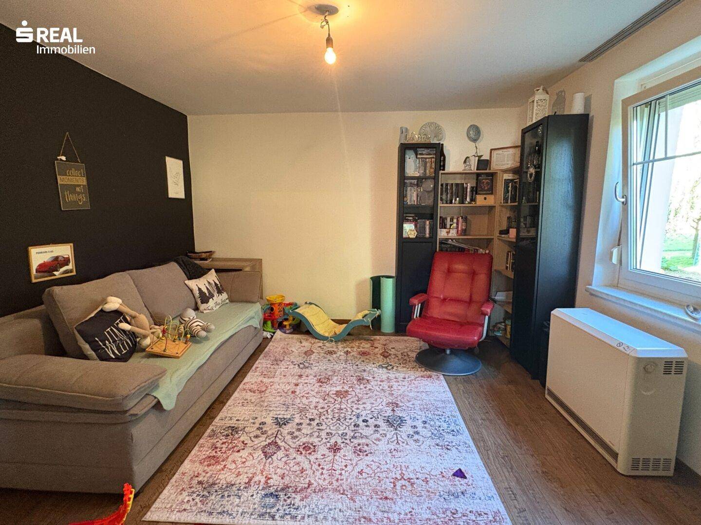 Gemütliches Wohnzimmer mit Sofa, Teppich und großem Fenster für viel Tageslicht.