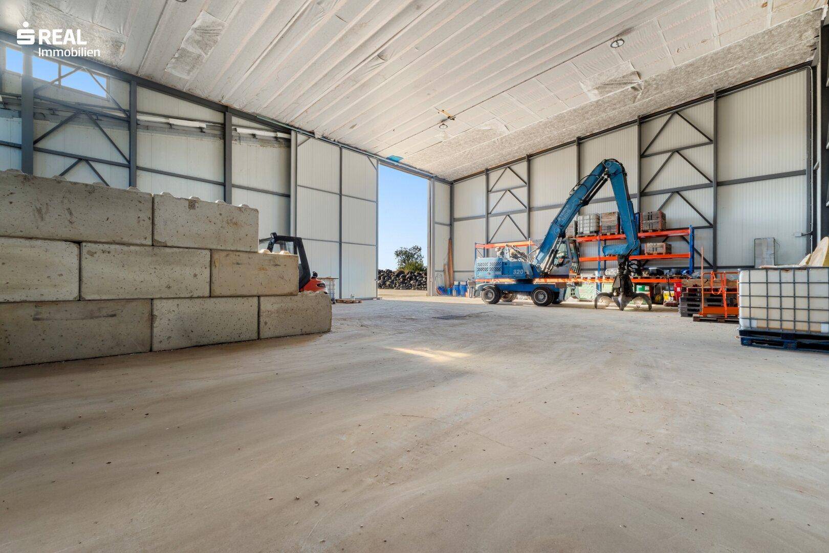 Weitläufige Lagerhalle mit Betonboden, Stahlkonstruktion und einem großen Rolltor.
