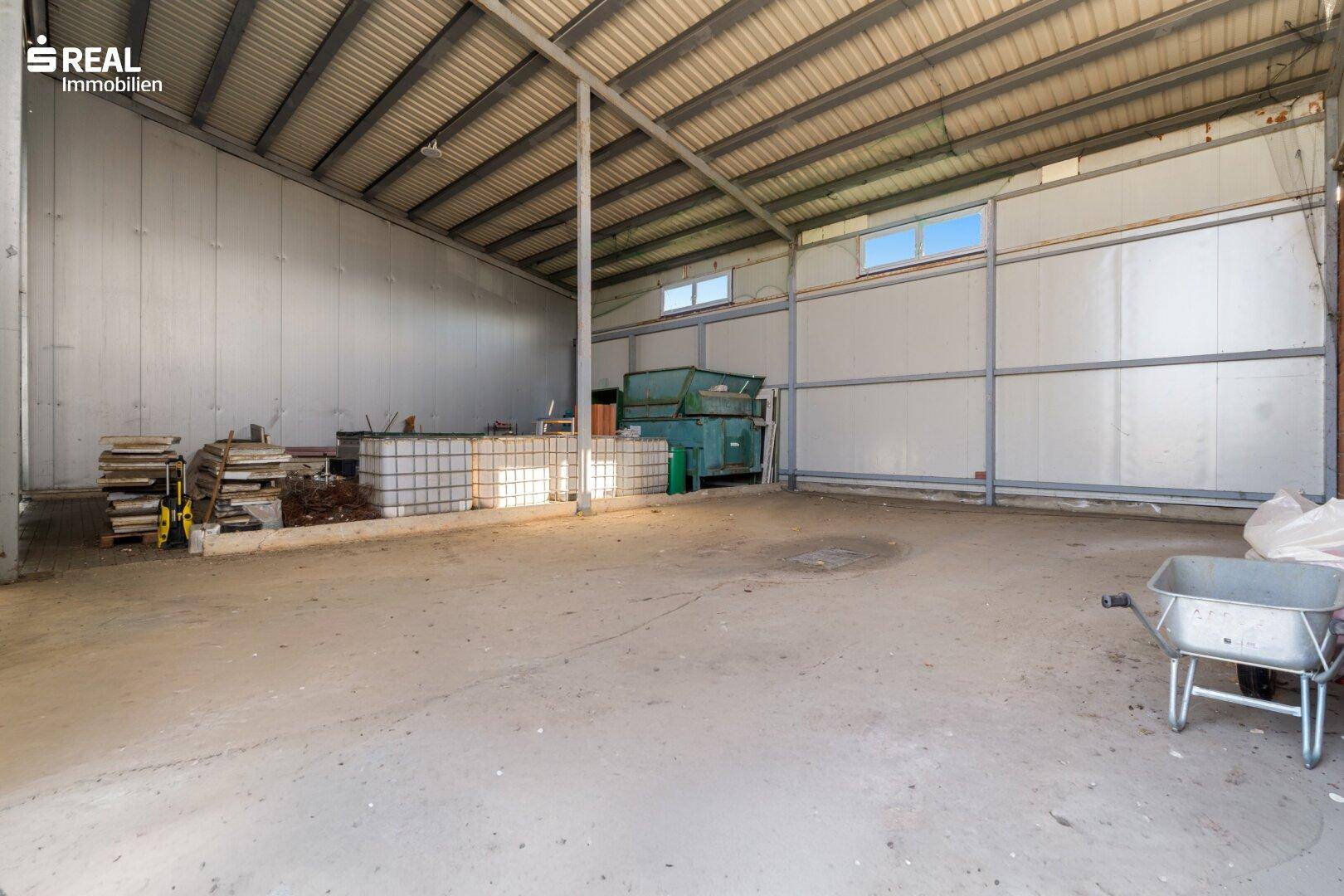 Leere Lagerhalle mit Betonboden, hohen Decken und einem Bereich für Abfallcontainer.