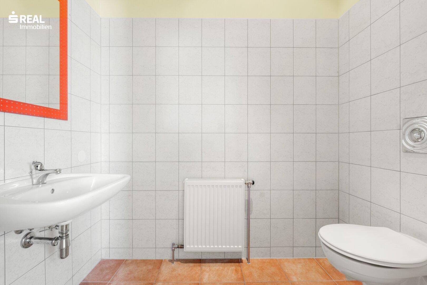 Sauberes Badezimmer mit Waschbecken, Toilette und weißer Fliesenwand, bereit zur Nutzung.