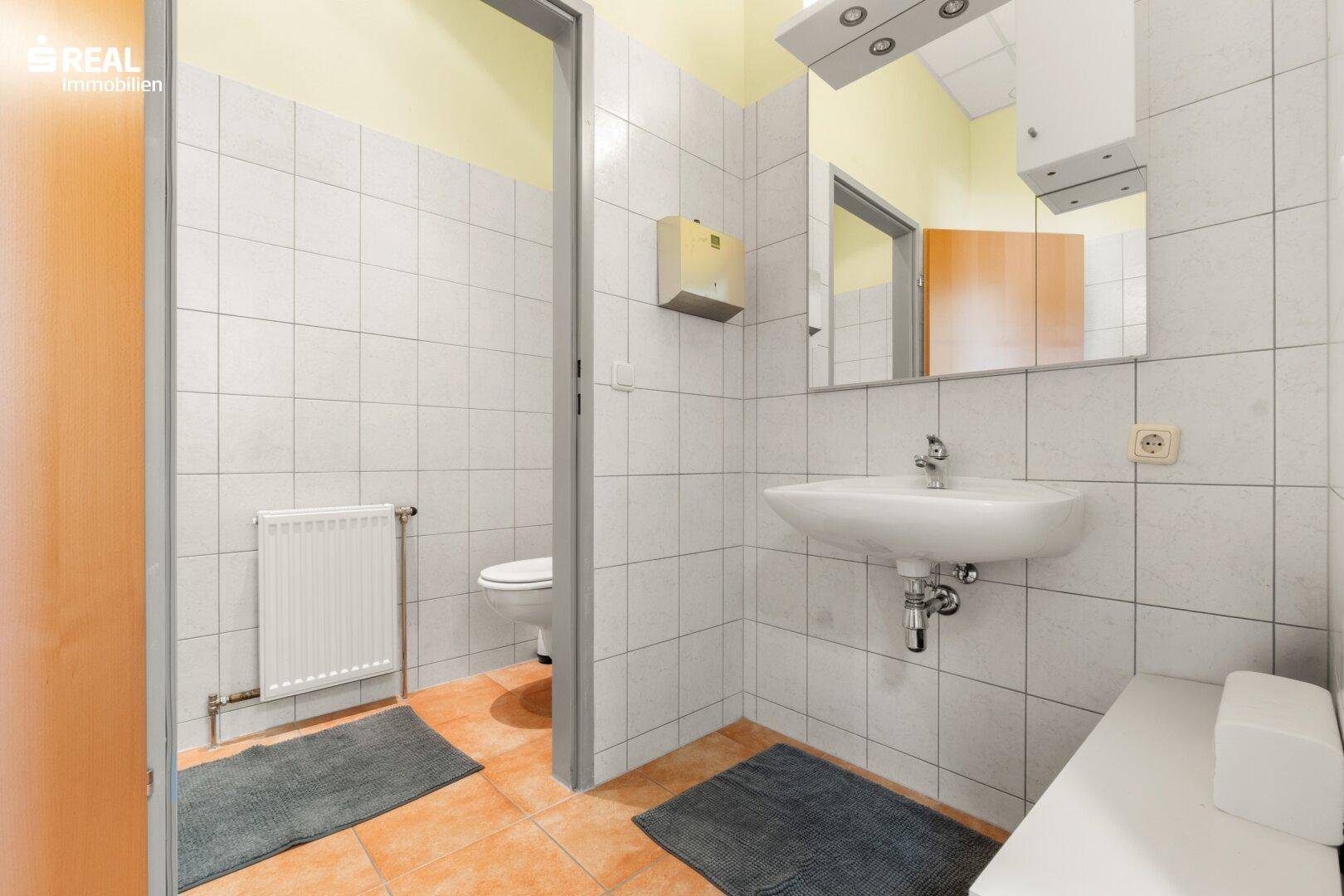 Gefliestes Badezimmer mit Waschbecken, Toilette und Heizkörper, in gutem Zustand.