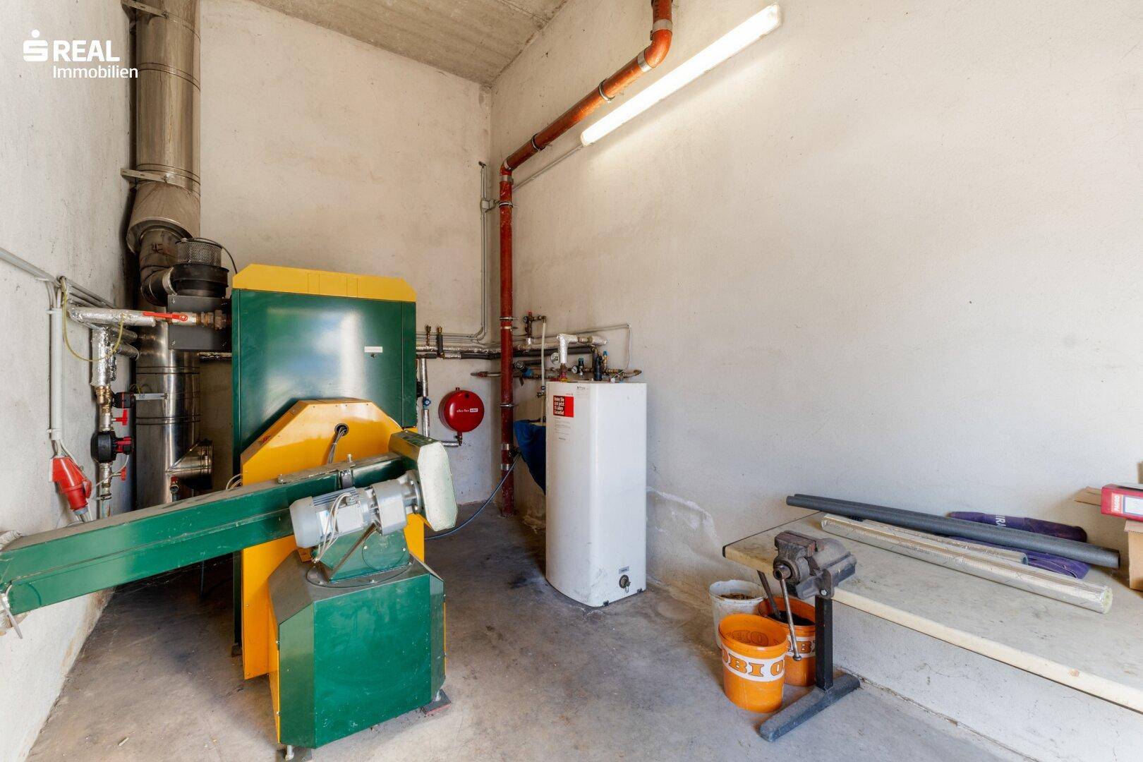 Technikraum mit Heizungsanlage, Warmwasserspeicher und sichtbaren Rohrleitungen.