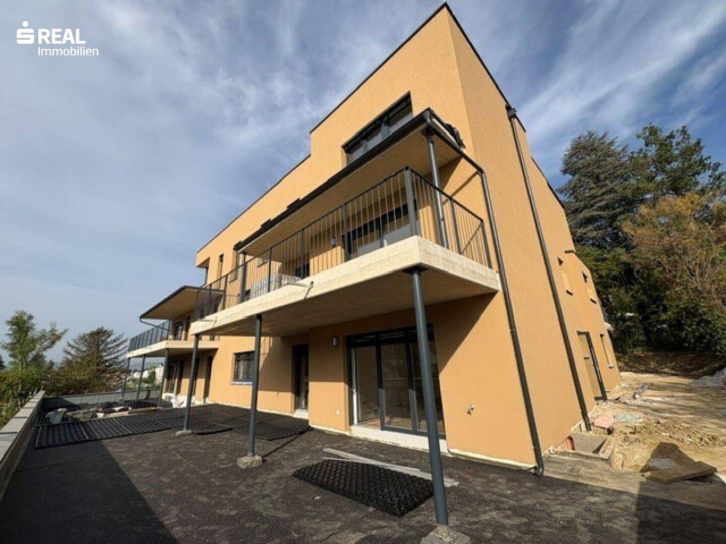 Modernes Mehrfamilienhaus mit Balkonen und einer großen, noch unfertigen Terrasse im Erdgeschoss.