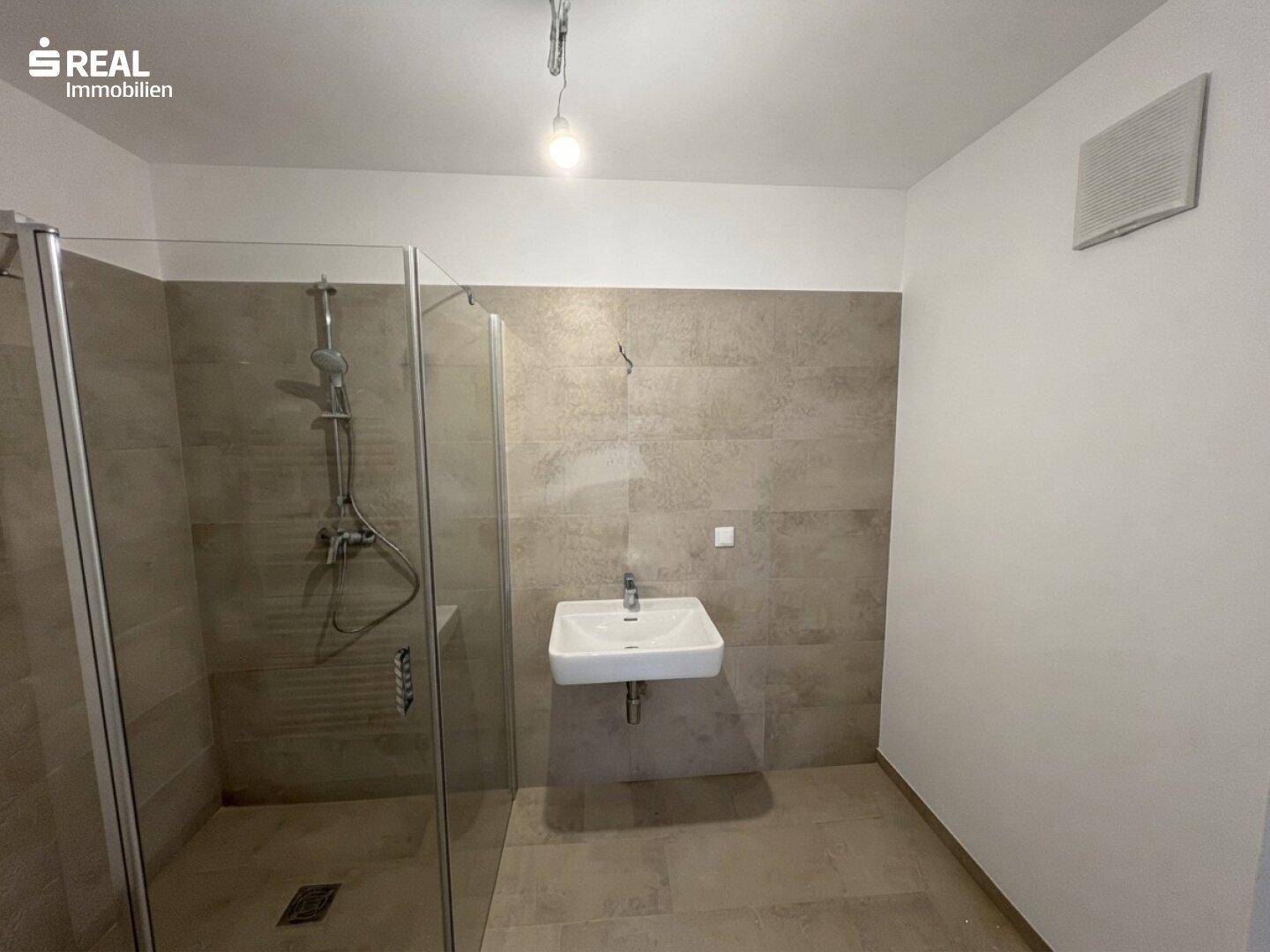 Modernes Badezimmer mit begehbarer Dusche, Wandwaschbecken und hellen Fliesen an Wänden und Boden.