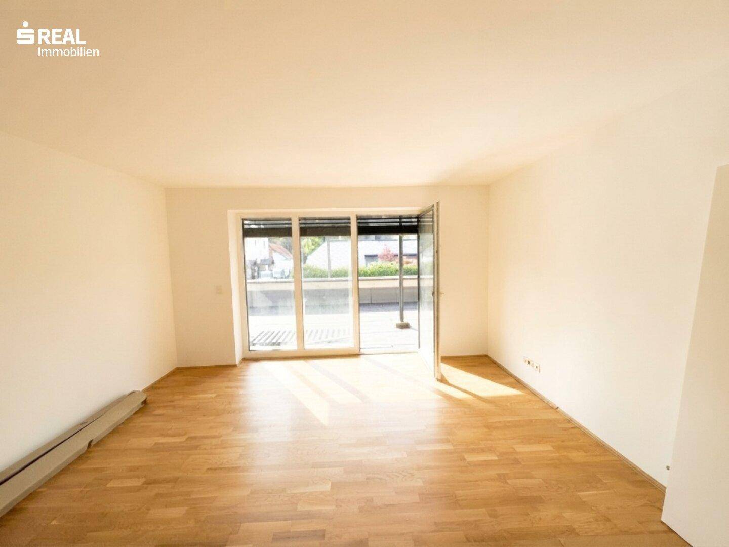Lichtdurchfluteter Wohnbereich mit hellem Parkettboden und breiter Schiebetür zur Außenterrasse.