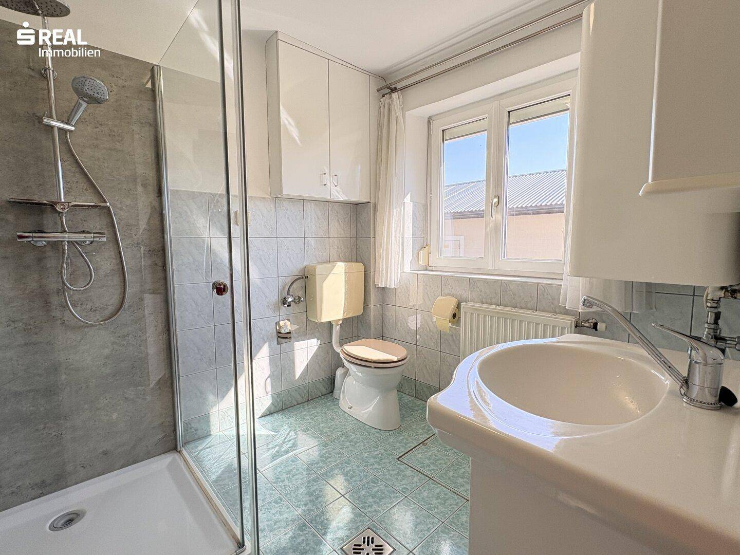 Helles Badezimmer mit Dusche, WC, Waschbecken und einem Fenster, das Tageslicht spendet.