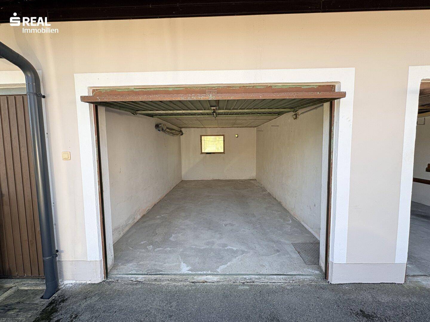 Leere Garage mit Betonboden und einem kleinen Fenster, bereit zur Nutzung und Lagerung.