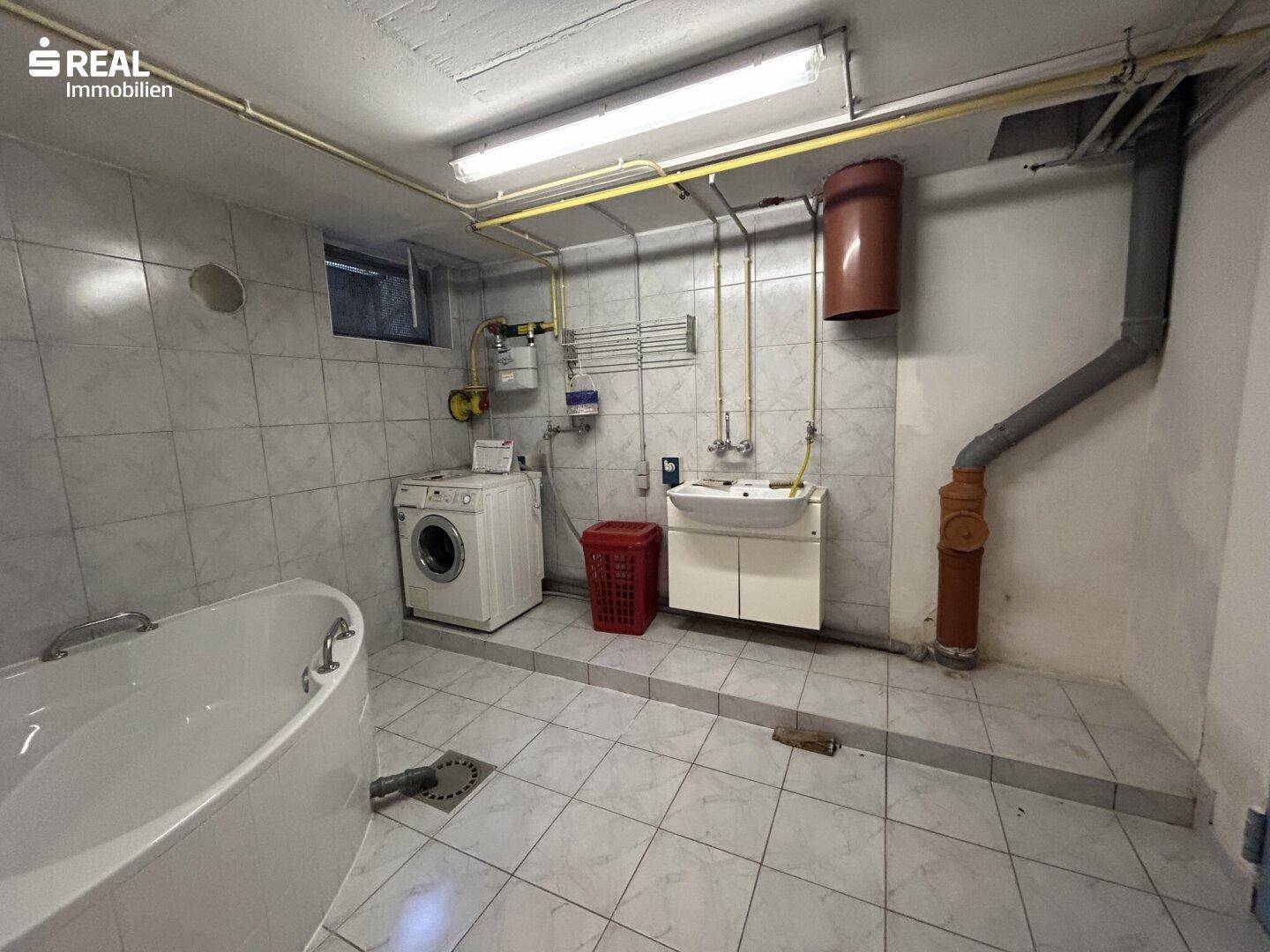 Funktionaler Waschraum im Keller mit Waschmaschine, Spülbecken und Badewanne.