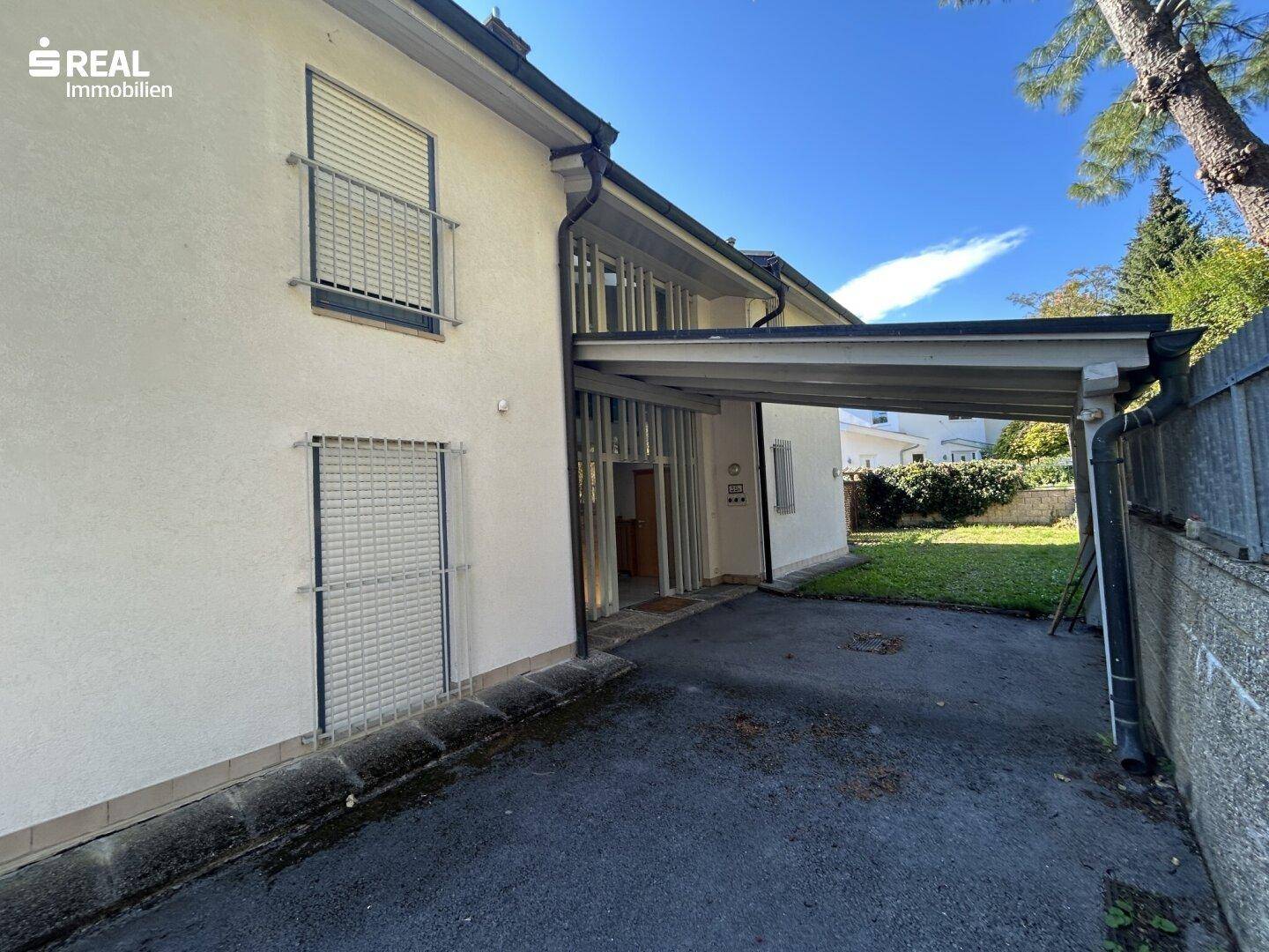 Seitenansicht des Hauses mit Carport, kleinen Balkonen und Rollläden an den Fenstern.