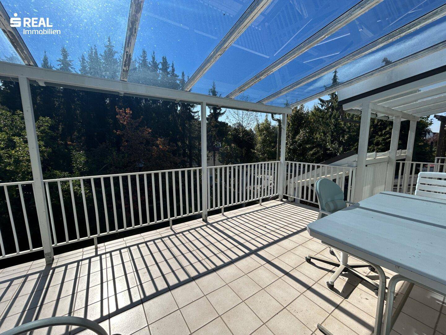 Überdachte Terrasse mit Fliesenboden, Gartenmöbeln und Blick ins Grüne.